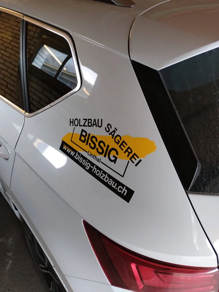 Fahrzeugbeschriftung Holzbau Bissig auf einer silbernen Heckklappe